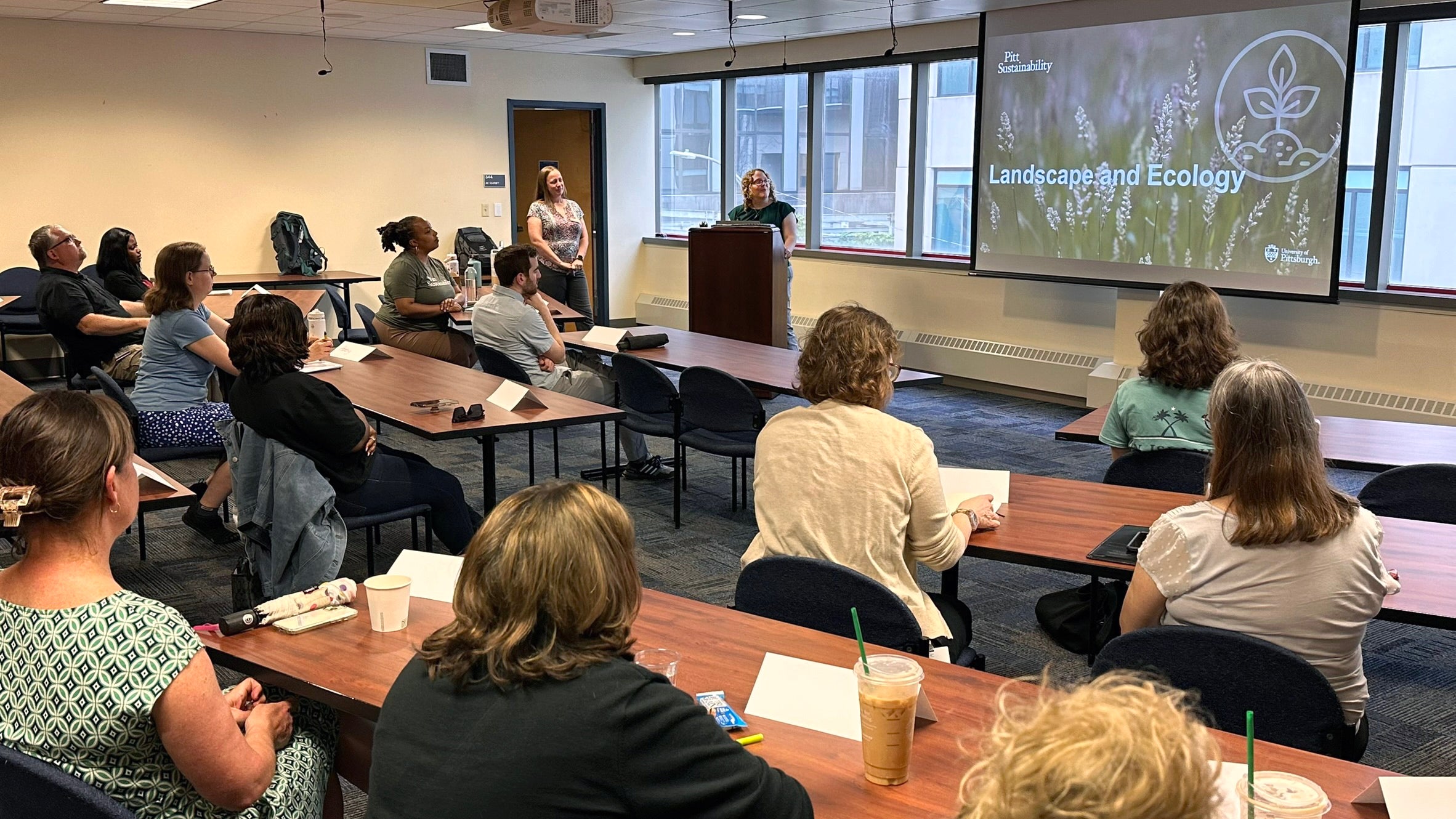 The instructor stands at a podium in front of the class, who are looking at a screen that reads "Pitt Sustainability: Landscape and Ecology"